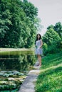 Young woman walking in the summer park. Woman in a green park near the pond. Beautiful woman in a colored sundress Royalty Free Stock Photo