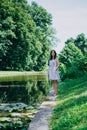 Young woman walking in the summer park. Woman in a green park near the pond. Beautiful woman in a colored sundress Royalty Free Stock Photo