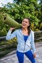 Young woman walking in urban park holding fitness rug. Royalty Free Stock Photo