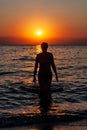 Young woman walking on water at sunset. Sunset and silhouette of a young woman as she emerges from the water. Royalty Free Stock Photo