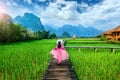 Young woman walking on wooden path with green rice field in Vang Vieng, Laos