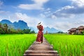 Young woman walking on wooden path with green rice field in Vang Vieng, Laos