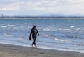 A young woman walks along the beach with running shoes in her hands, she walks barefoot along the sea. White Rock,BC