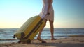 Young woman walks along the beach of the sea with a yellow suitcase closeup. A girl in a white dress walks barefoot on Royalty Free Stock Photo