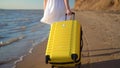 Young woman walks along the beach of the sea with a yellow suitcase closeup. A girl in a white dress walks barefoot on Royalty Free Stock Photo