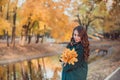 A young woman walks in the autumn Park. She stands by the lake. Brunette woman wearing a green coat