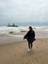 Young woman walks at the beach near sunken trawler, shipwreck. Old ship Zeila.