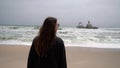 Young woman walks at the beach near sunken trawler, shipwreck. Old ship Zeila.