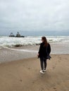 Young woman walks at the beach near sunken trawler, shipwreck. Old ship Zeila.