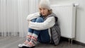 Young woman in warm clothes sitting at broken heating radiator in house. Concept of energy crisis, high bills, broken heating Royalty Free Stock Photo