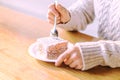 A young woman in a warm knitted sweater uses a teaspoon to cut a piece of delicious cake in a cafe on a brown wooden table. Cup of