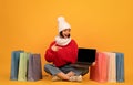 Young woman in warm outfit showing laptop empty screen, pointing finger on it and sitting among colorful shopping bags Royalty Free Stock Photo