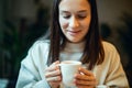 Young woman in warm sweater holding cup of coffee and planing personal goals for new year.