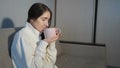 Young woman in warm sweater sitting on sofa and and drinking tea at home Royalty Free Stock Photo