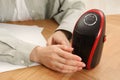 Young woman warming hands near compact electric heater at wooden table, closeup Royalty Free Stock Photo