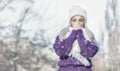 Young woman warming her hands, wearing warm clothing on snowing winter day outdoors. Cute girl feeling cold. Winter concept