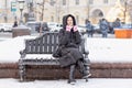 A young woman warmly dressed is sitting on a bench in the city on the street on a snowy cold day Royalty Free Stock Photo