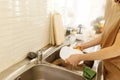 young woman washing dishes in the kitchen sink at home, close up of hands with sponge and soap, housework, copy space Royalty Free Stock Photo