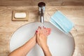 Young woman rinsing off the soap from her hands under tap water during pandemia