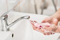 Young woman washing her hands under water tap faucet with pink soap bar. Detail on suds covered skin. Personal hygiene concept - Royalty Free Stock Photo
