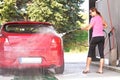 Young woman washing her red car in self serve carwash, view from back