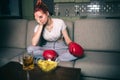 Young woman watch boxing on tv at night. Confused upset and unhappy model hold hand on face. Alone in room. Jink food on