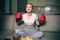 Young woman watch boxing on tv at night. Happy joyful model look up forward and smile. Cheering. Sport boxing gloves on