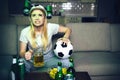 Young woman watch football game on tv at night. Intence play. Worry model sit on sofa and hold glass of beer and ball Royalty Free Stock Photo