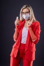 A young woman with watch in her hand and a mask on her face warns of danger by gesturing with her index finger