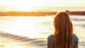 Young woman watches sunset over sea at the beach, view from back, detail on her hair, wide banner with space for text left