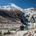 Young woman watching beautiful view of Manaslu mountain range, Birendra lake. Lady sits in front of snow covered Mount Manaslu