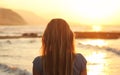 Young woman watching sunset at the beach, looking to sea, mountains in distance. View from back, only her head and hairs visible