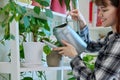 Young woman watering pots with plants from watering can, home interior Royalty Free Stock Photo