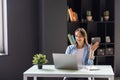 Young woman waving hello talking on a video call. Successful young woman sitting at business workspace. Business conference via