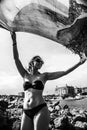 Young woman waving scarf in wind at beach. Happy woman in red bikini holding tissue and looking away at sea.