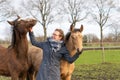 Young woman in a wax coat with her two 1 year old stallions in the pasture. Two curious horses heads