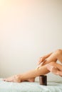 Young woman depilating legs with wax sitting on bed Royalty Free Stock Photo