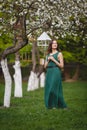 Young woman weared in long green dress in a blooming apple garden