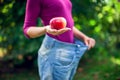 Young woman wearing big loose jeans with apple in hand - weight Royalty Free Stock Photo