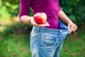 Young woman wearing big loose jeans with apple in hand - weight Royalty Free Stock Photo