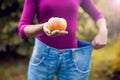 Young woman wearing big loose jeans with apple in hand - weight Royalty Free Stock Photo