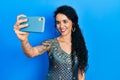 Young woman wearing bindi and traditional kurta dress taking a selfie photo with smartphone looking positive and happy standing Royalty Free Stock Photo