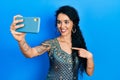 Young woman wearing bindi and traditional kurta dress taking a selfie photo with smartphone smiling happy pointing with hand and Royalty Free Stock Photo