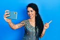 Young woman wearing bindi and traditional kurta dress taking a selfie photo with smartphone smiling happy pointing with hand and Royalty Free Stock Photo