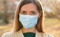 Young woman wearing blue disposable mouth nose mask, nice sunny bokeh in background, closeup face portrait Royalty Free Stock Photo