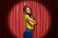 Young woman wearing blue jeans and yellow shirt embracing herself on red stage curtains background Royalty Free Stock Photo