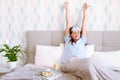 Young woman wearing blue pajanas and sleeping mask waking up happily after a good night sleep with her hands up Royalty Free Stock Photo