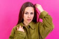 Young woman wearing a brown coat standing with her hand on her head on a pink background Royalty Free Stock Photo