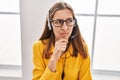 Young woman wearing call center agent headset serious face thinking about question with hand on chin, thoughtful about confusing Royalty Free Stock Photo