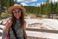 Young woman wearing a camoflauge outfit and sun hat poses at the mud pots at Artist Paint Pots in Yellowstone